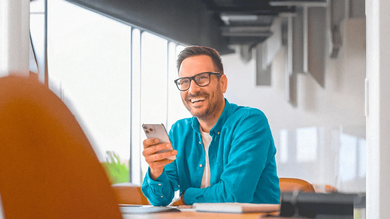 Homem sorridente usando o celular em um ambiente de trabalho, representando uma experiência de compra digital simples e fluida.